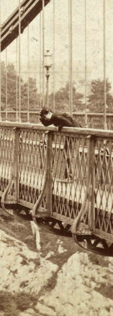 A little Victorian boy leans over the side of the bridge